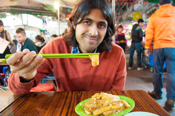 Ashray eating garlic fried eggplant at a night market in Kow Loong